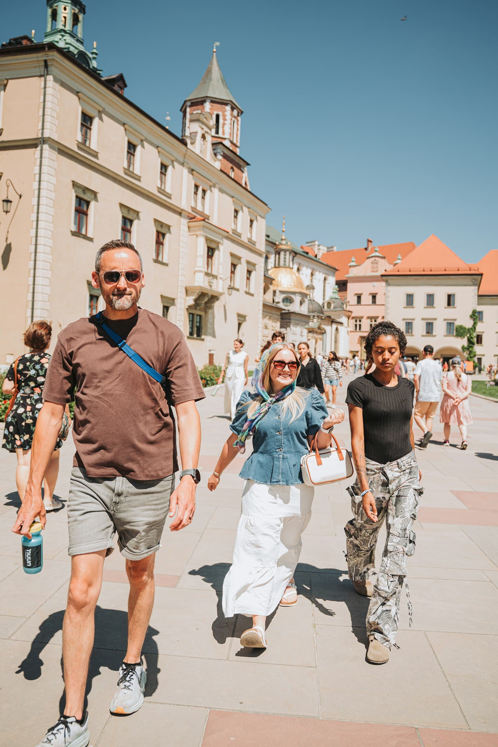 Three people walking together on a sunny street lined with historic buildings